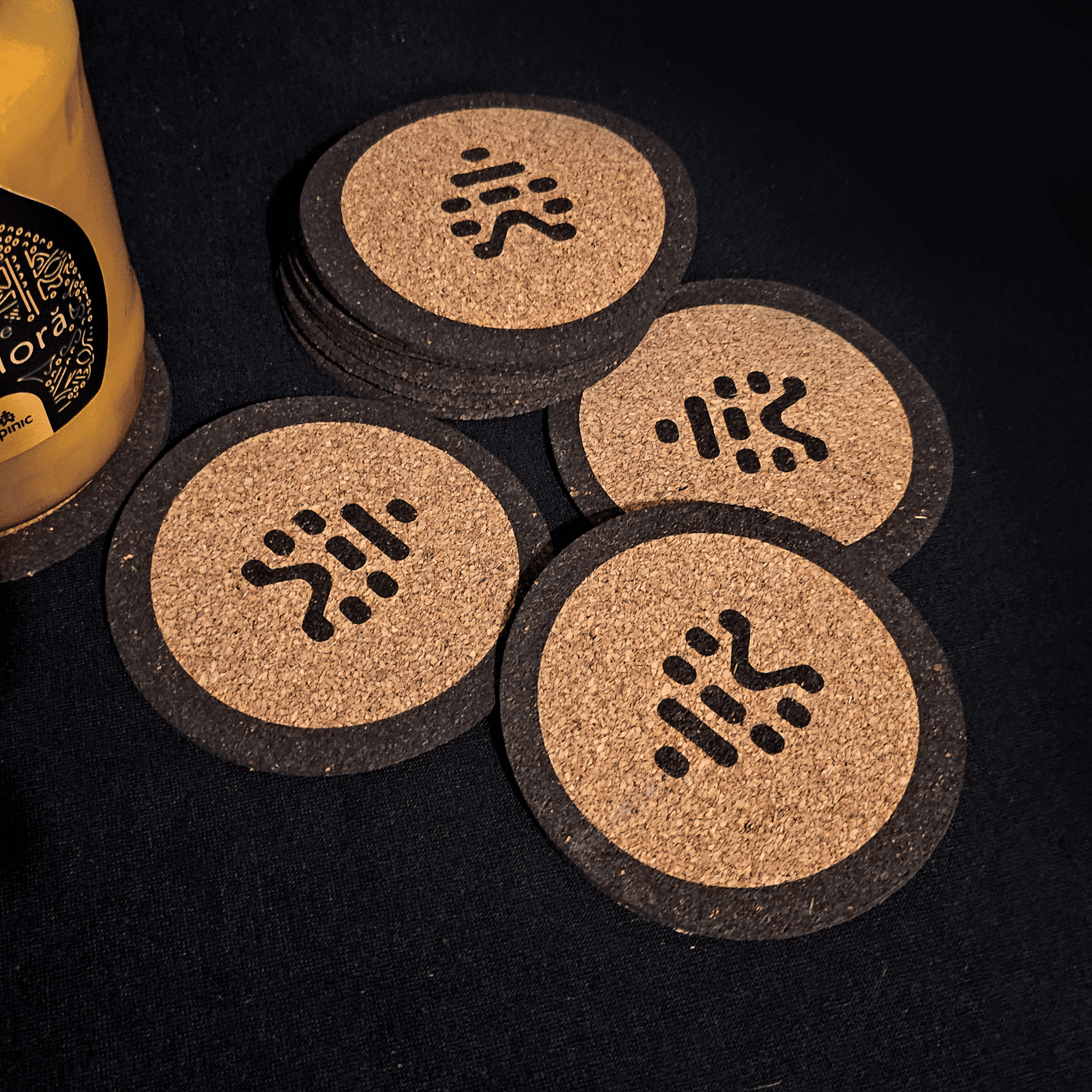 Close-up image showing a collection of round coasters with a black and beige design on a dark surface, alongside a yellow object partially visible on the left side.