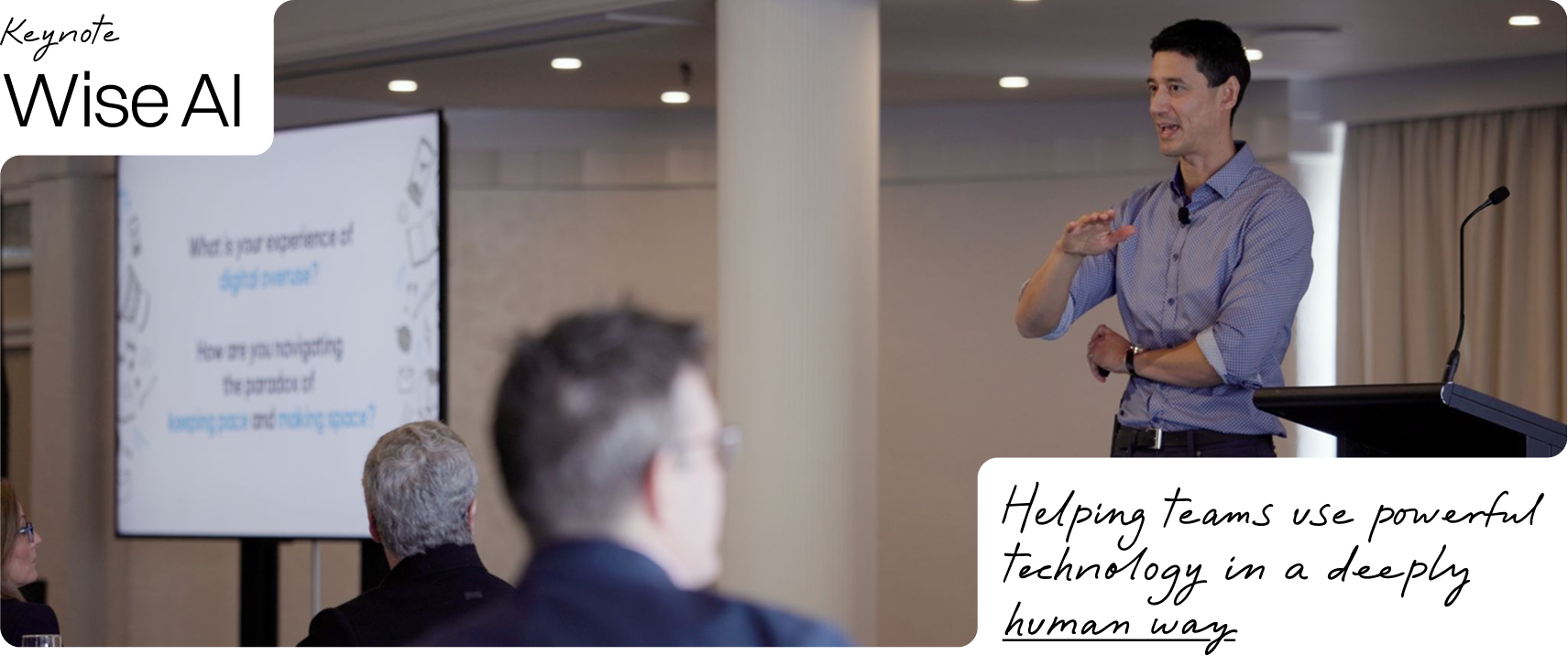 A man giving a presentation at a conference with a screen behind him displaying a slide titled 'What is your experience of digital overload?' and the question 'How are you managing the paradox of keeping pace and making space?'. The audience is seated, and the room has a modern, professional appearance.