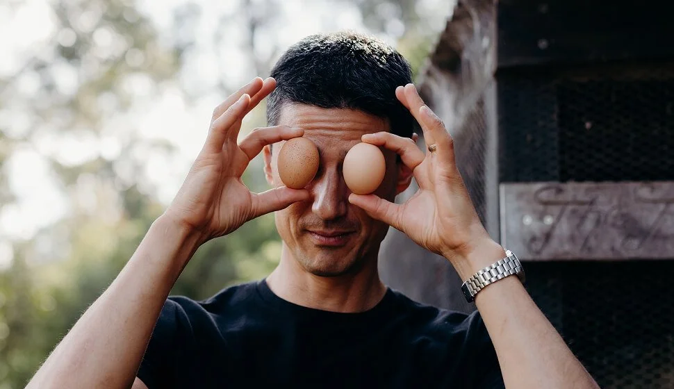 A man holding two eggs in front of his eyes in an outdoor setting.
