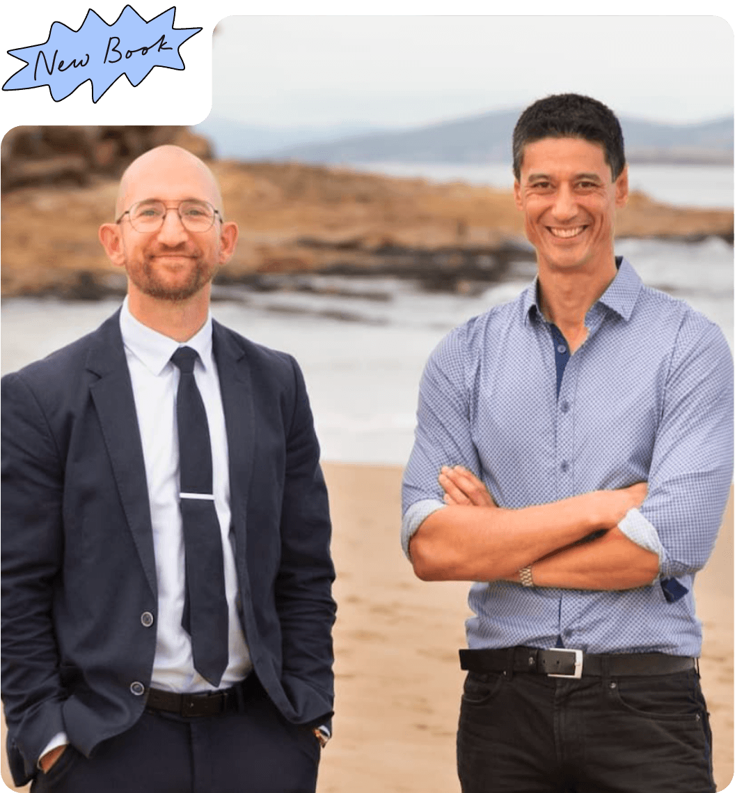 Paul Matthews and Daniel Sih posed at the beach. Paul wears a navy suit and light blue shirt, while Daniel wears a patterned blue shirt.