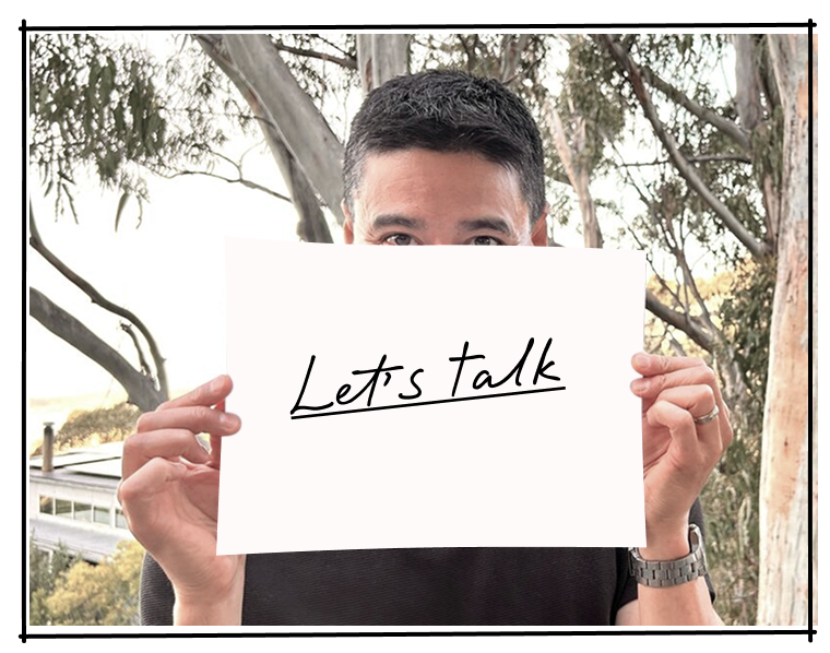 Daniel outdoors holding a piece of paper that says 'Let's Talk'