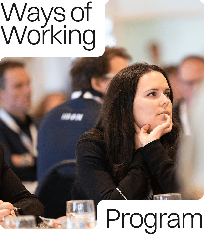 A female with dark hair sitting at a table listening. Male colleagues sit in the blurred background.