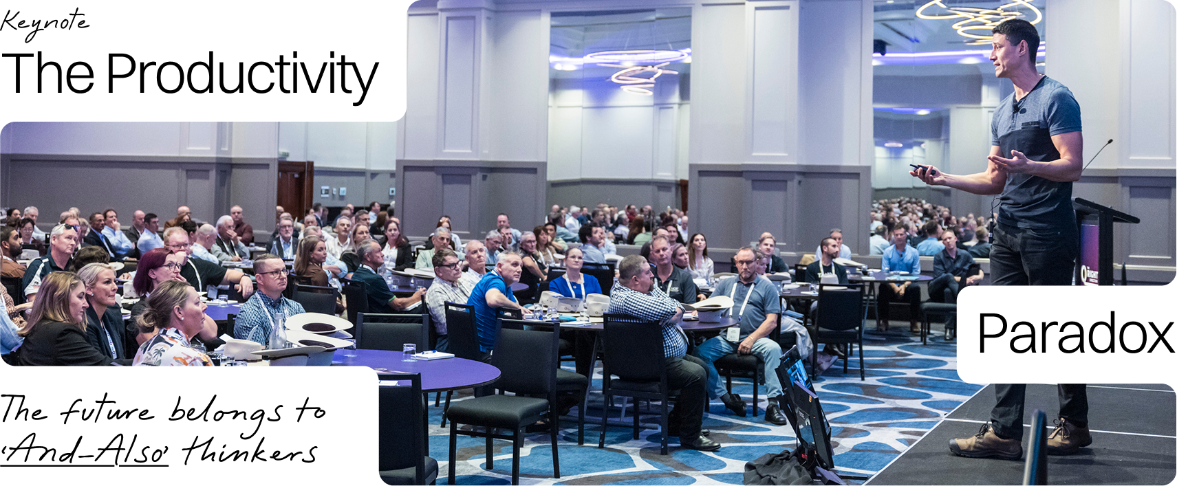 A man giving a presentation to a large audience in a conference room with modern lighting and patterned carpet.