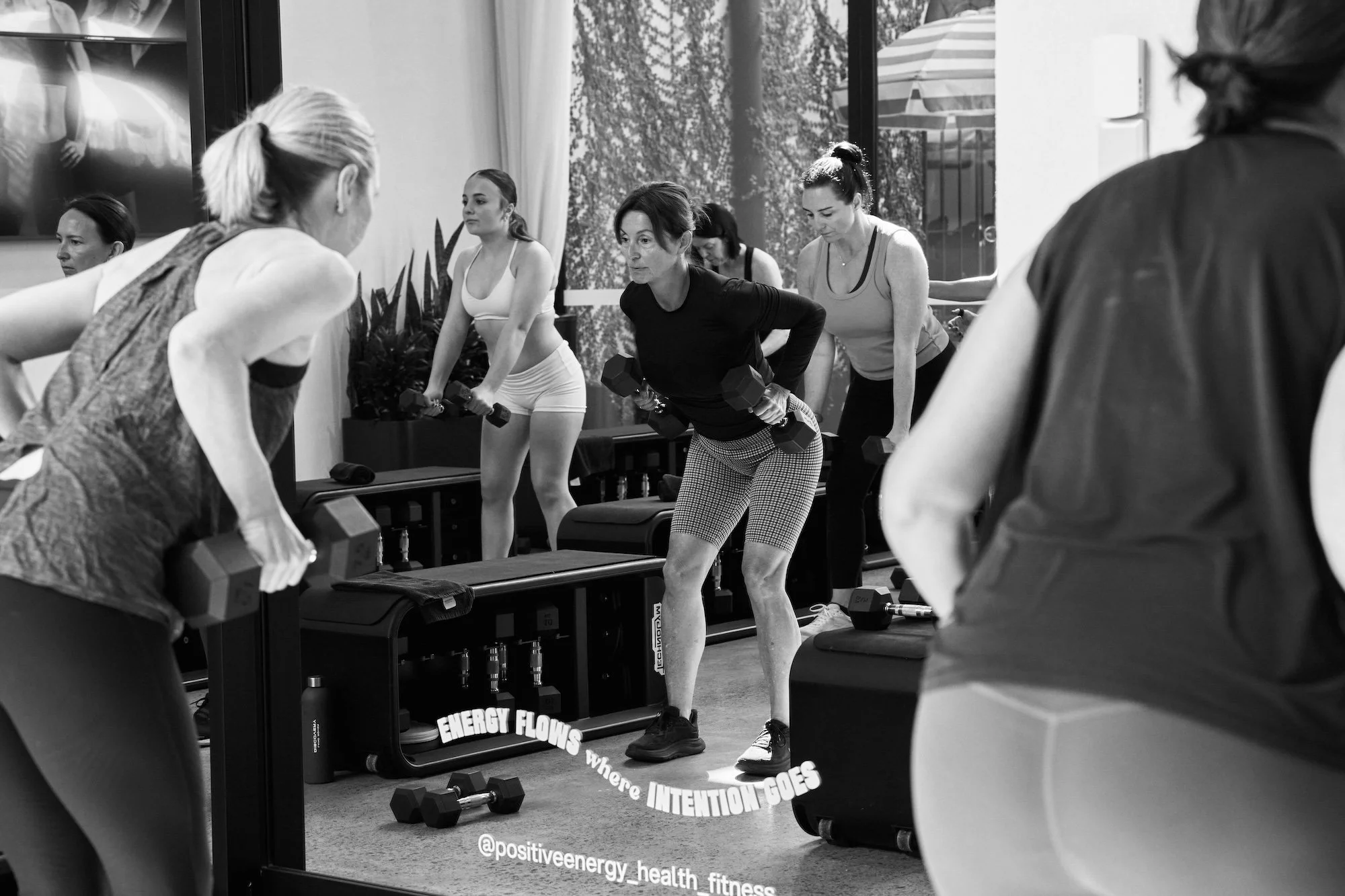 Women working out with dumbbells in a fitness class at a gym, reflecting in a mirror