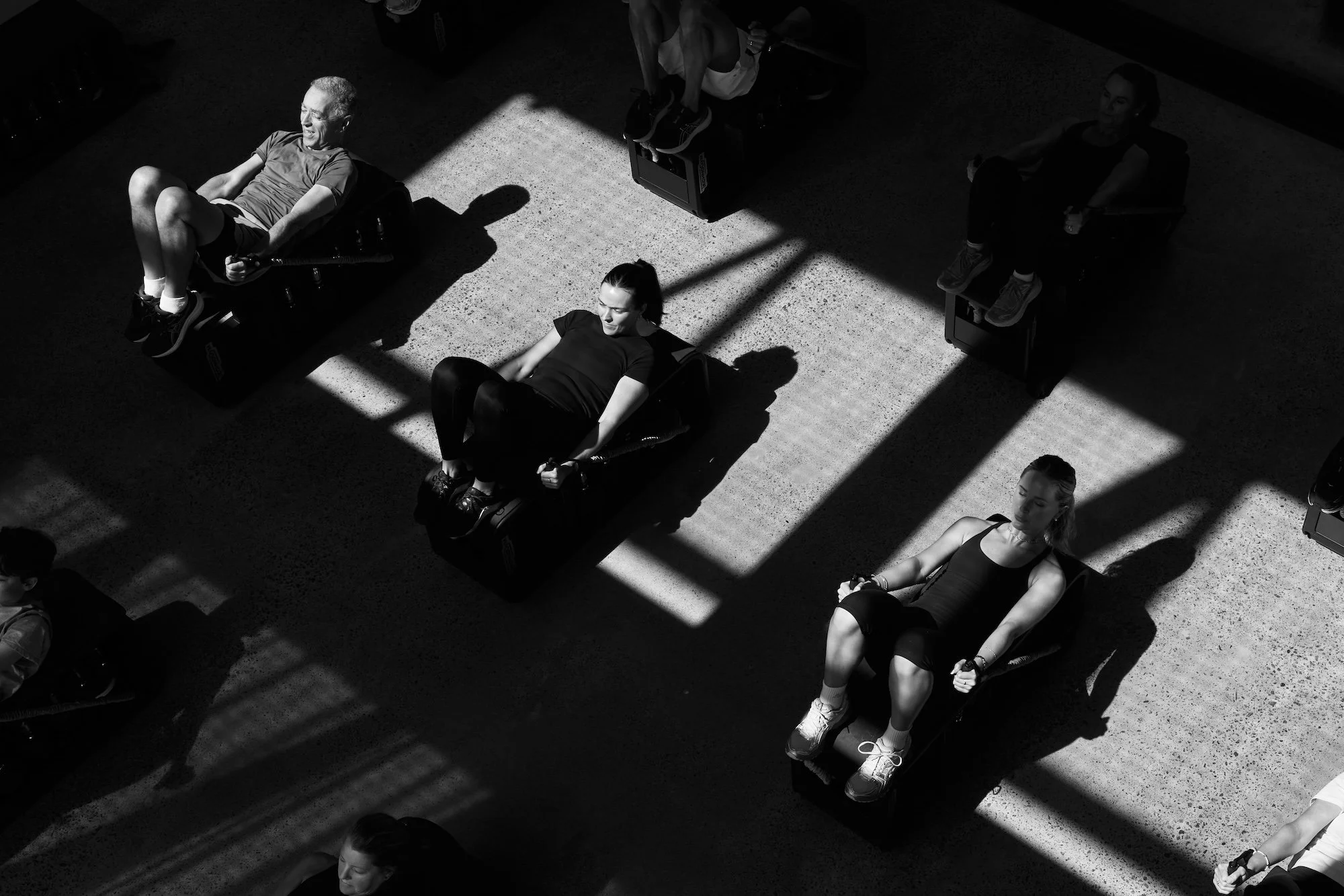People sitting on chairs in a room with sunlight casting shadows through large windows, creating patterns on the floor.