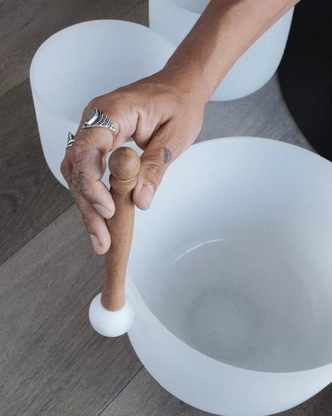 A person with rings on their fingers holding a wooden mallet over a white ceramic bowl.