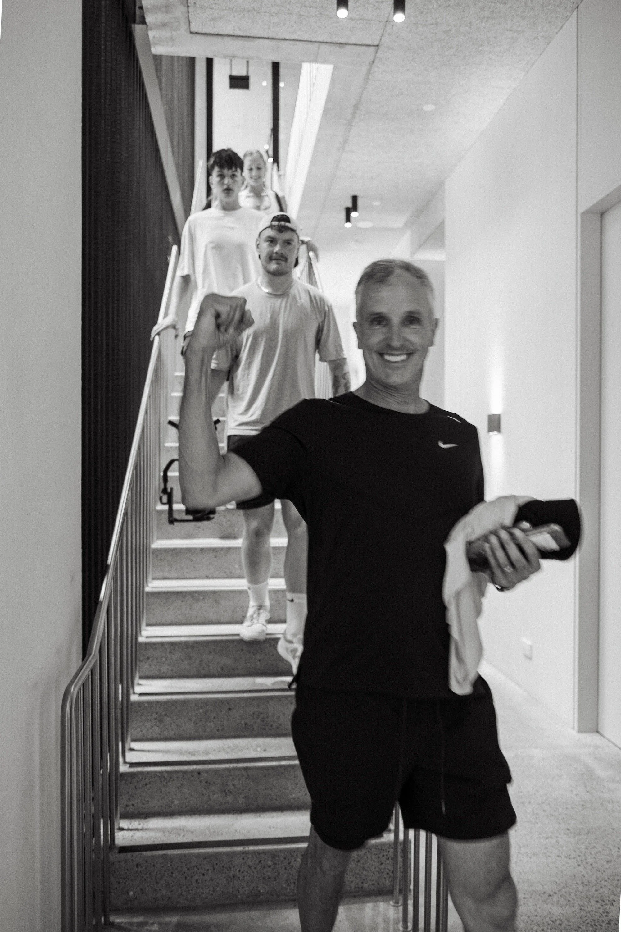A man taking a selfie with four people walking down a staircase behind him in an indoor setting.