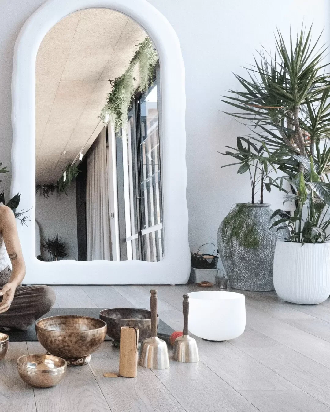 Interior space with a large white-framed mirror, potted plants, and singing bowls on the floor.