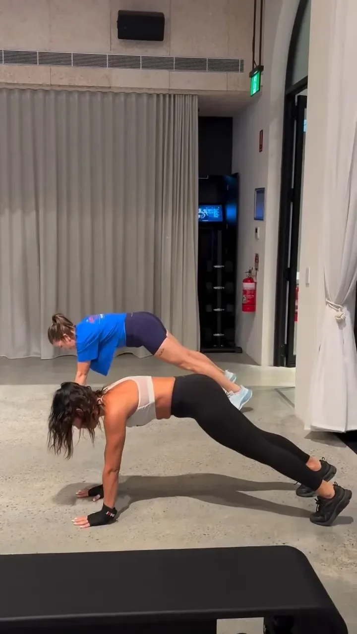 Two women exercising indoors, with one in a push-up position and the other in a plank position on her hands and feet.