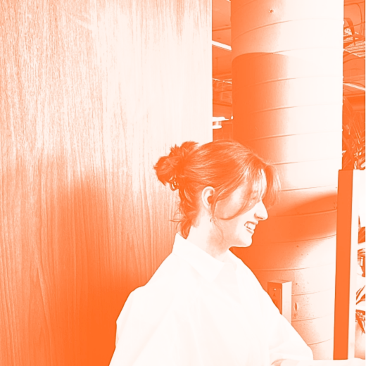 A woman with brown hair in a messy bun smiling while looking at her phone in a modern indoor setting.
