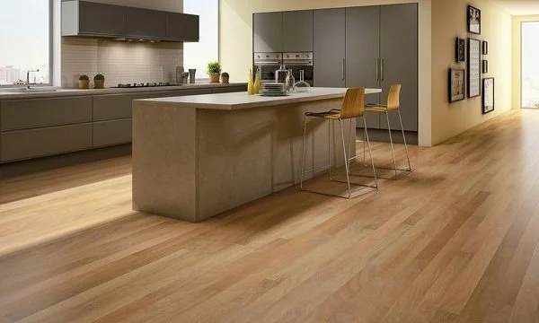 Cocina moderna con isla de color gris, encimeras claras, gabinetes grises y sillas de madera en una encimera elevada, con paredes en tonos neutrales y suelo de madera clara.