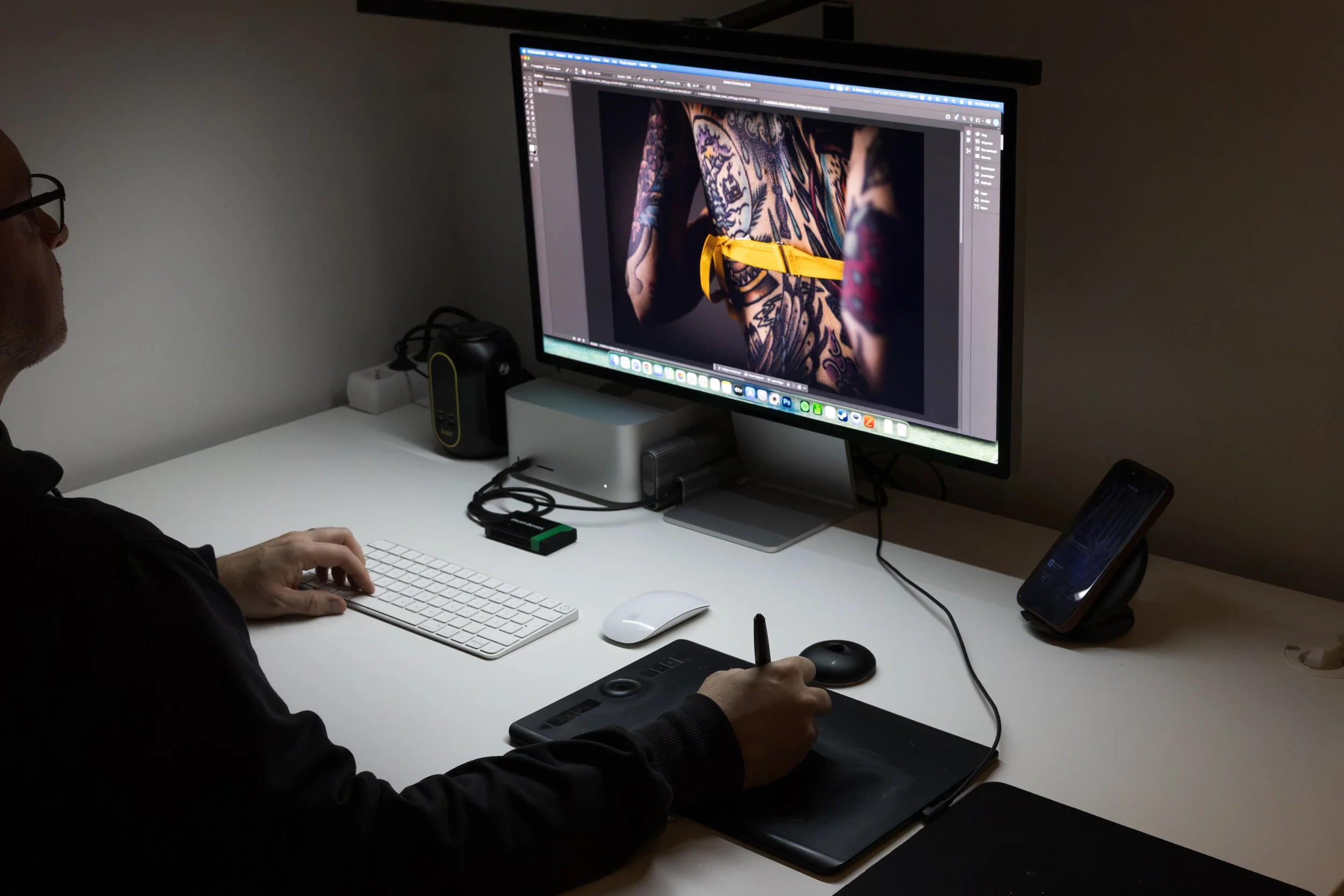 Person som ritar med en digital penna på ett ritplatta framför en dator med en skärm som visar en tatuerad kvinna därbilden redigeras i Photoshop