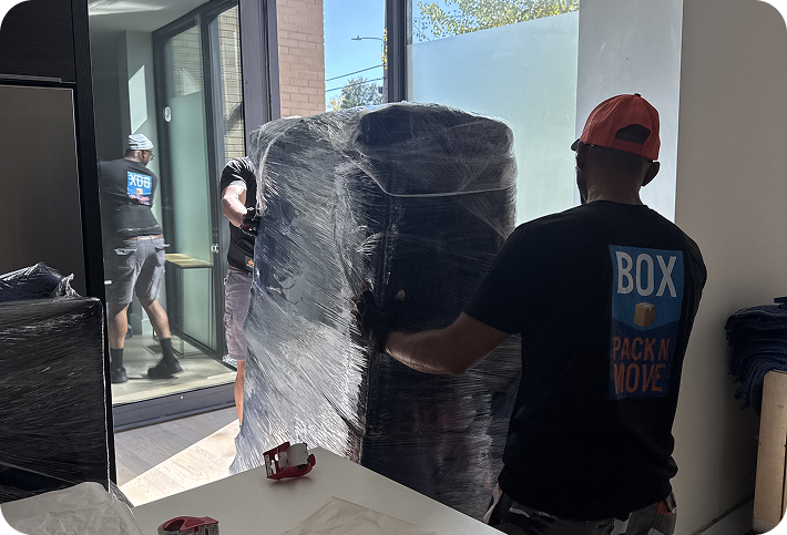Movers carrying a wrapped heavy item through a doorway