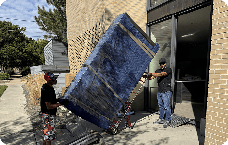 Movers transporting wrapped furniture on a dolly