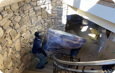 Piano movers carrying a wrapped piano downstairs