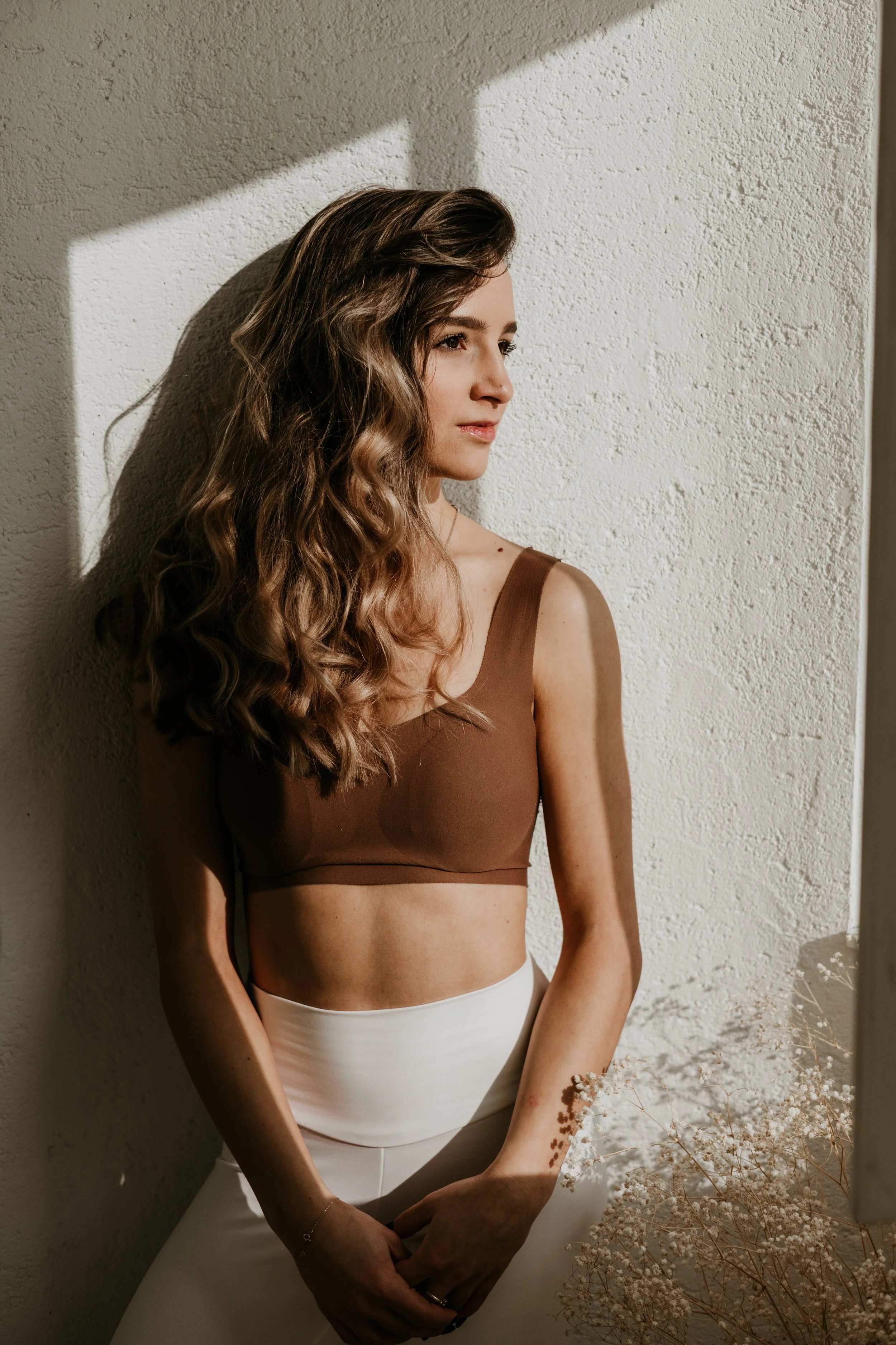 A woman with wavy, brown hair wearing a brown crop top and white pants