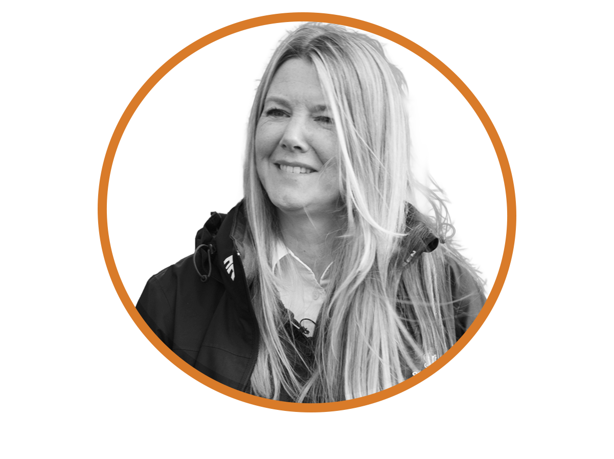 Black and white photo of Charlotte Worden of SHC smiling with long blonde hair, wearing outdoor clothing, on an orange and black graphic background.