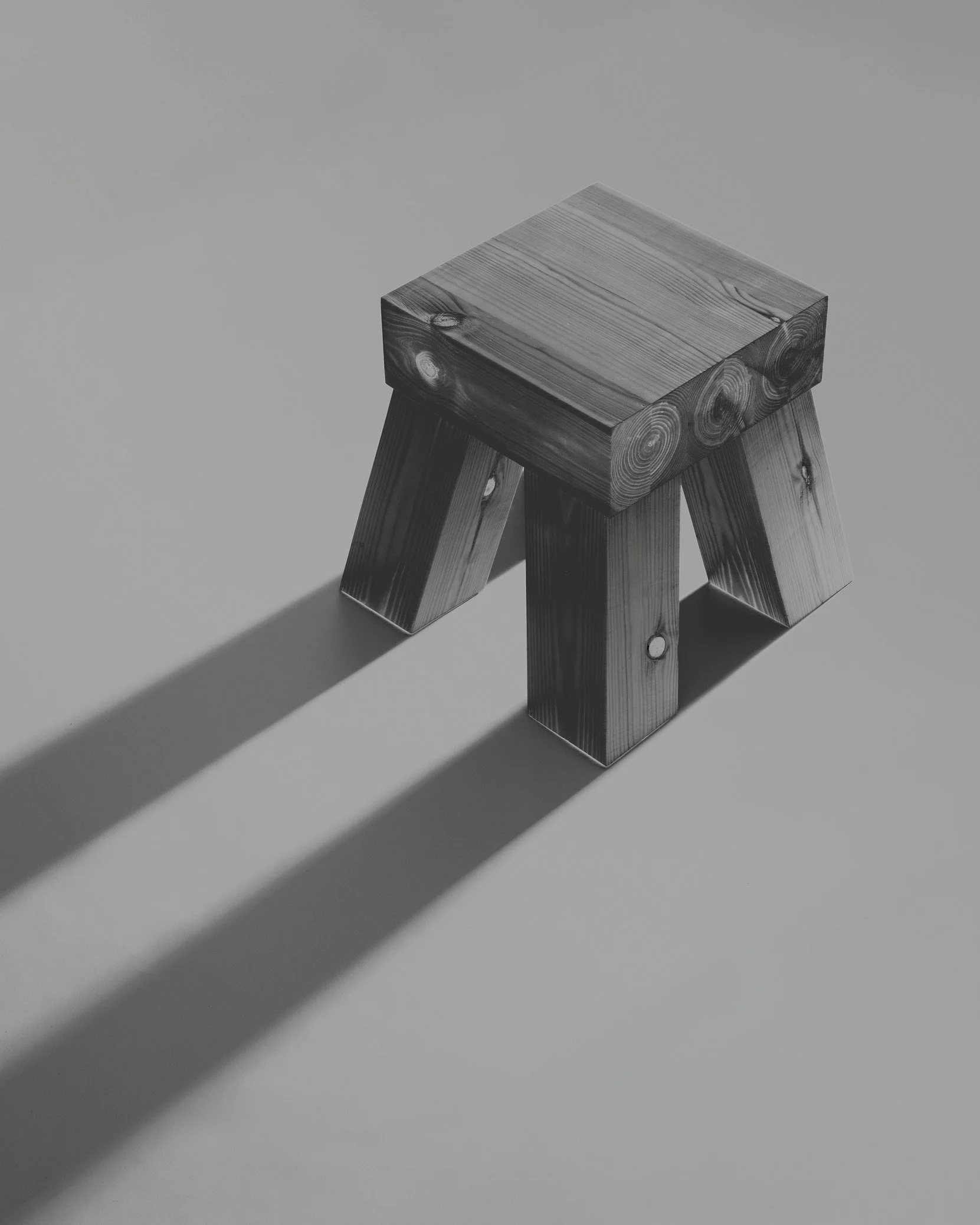 A wooden stool with three legs casting a shadow on a plain surface.