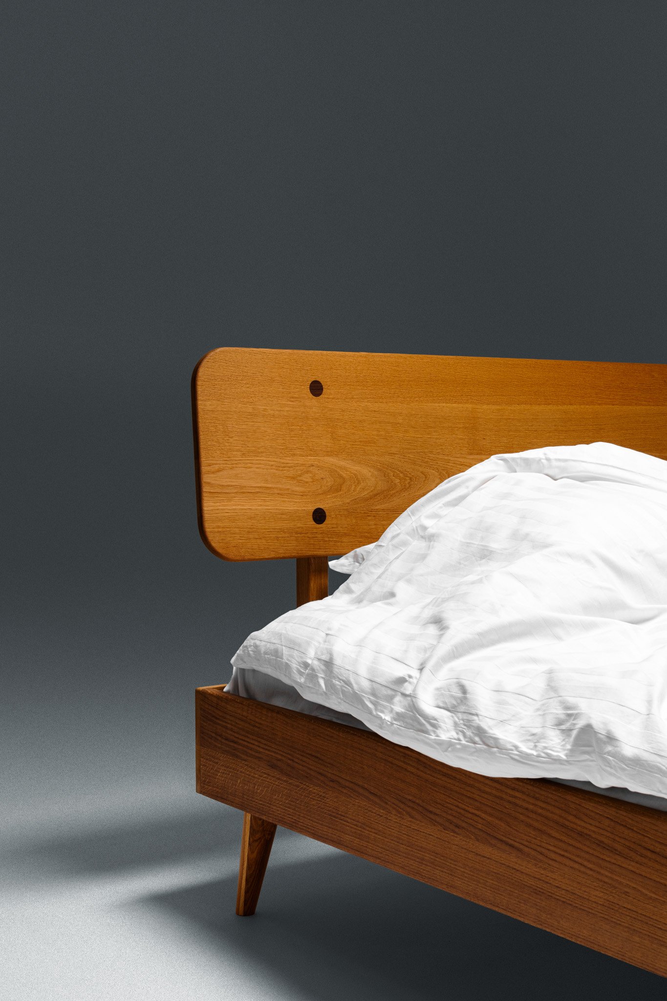 A wooden bed with a white pillow and white bedding, set against a plain gray wall.