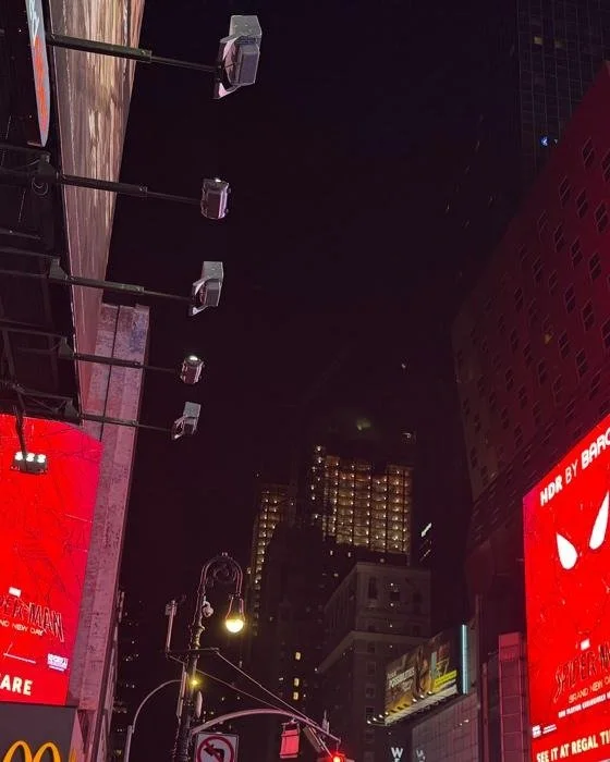 Rigging and mounting hardware on the Times Square billboard structure with red-lit signage in the background