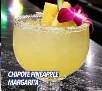 Cóctel Chipotle Pineapple Margarita con rodaja de piña y flor en el borde