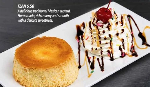 Un flan tradicional mexicano con una capa dorada en la parte superior, acompañado de una porción de crema batida decorada con jarabe de chocolate, caramelo y una cereza en la parte superior, servido en un plato rectangular blanco.