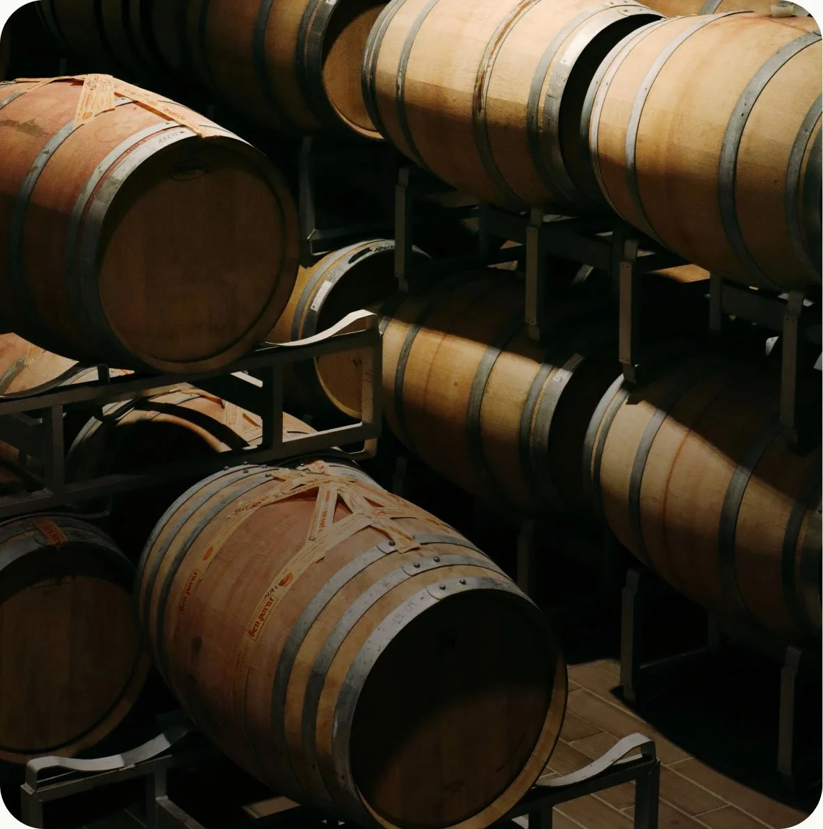 Wine barrels stored on metal racks in a cellar with wooden flooring.