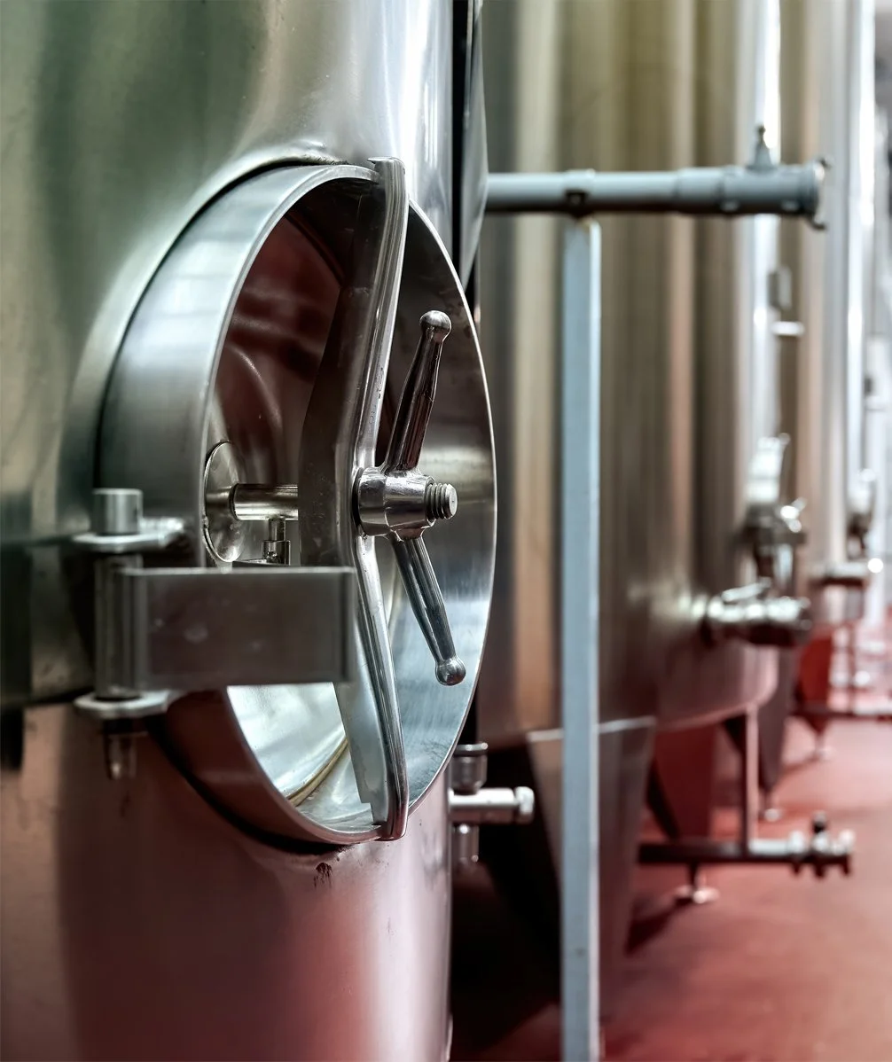 Close-up of a large stainless steel industrial fermentation tank with a wheel valve in a brewery or dairy facility.