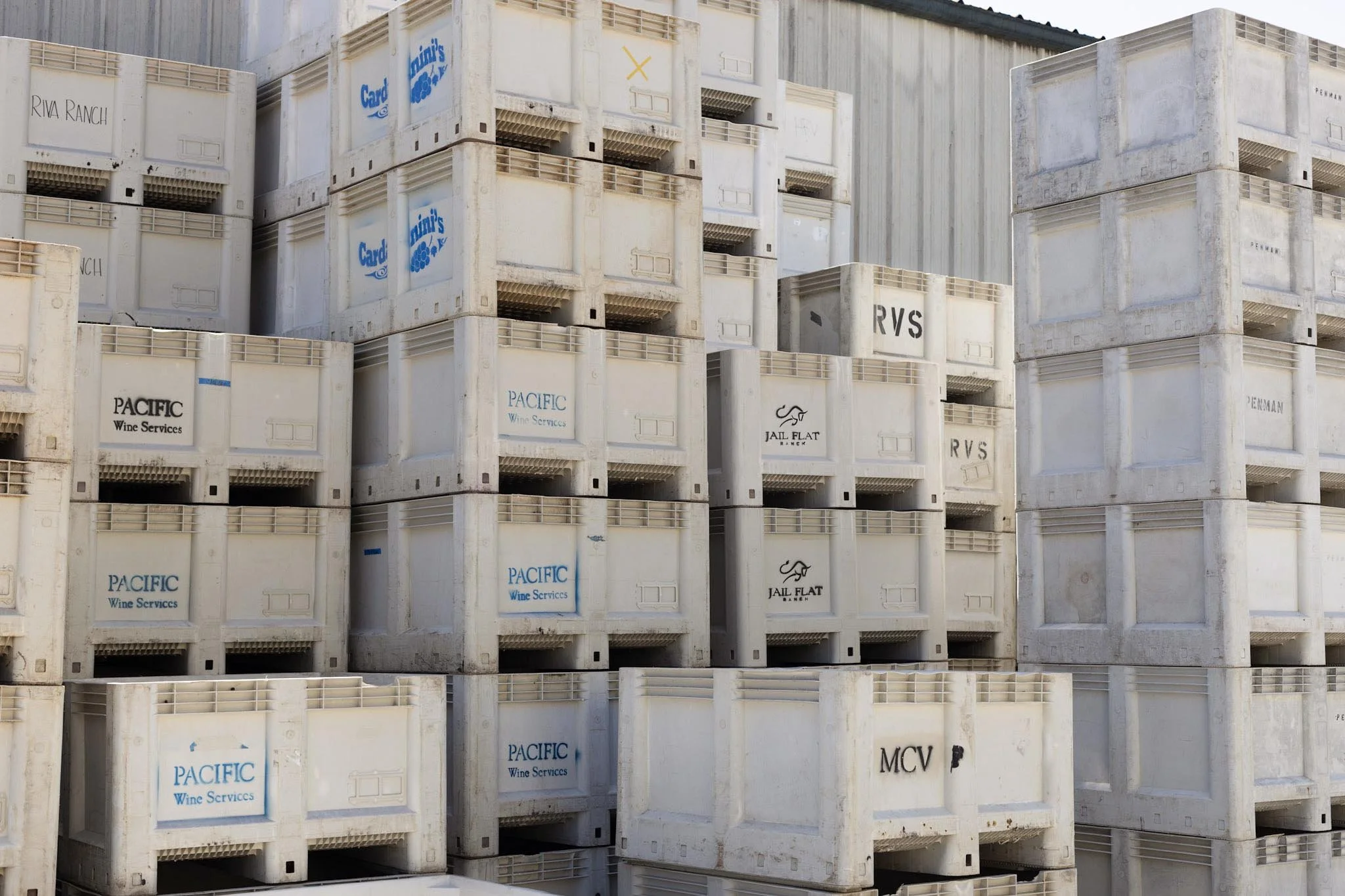 Stacks of white plastic crates with labels including 'Pacific Wine Services,' 'Riva Ranch,' and 'Jail Flat Ranch'.
