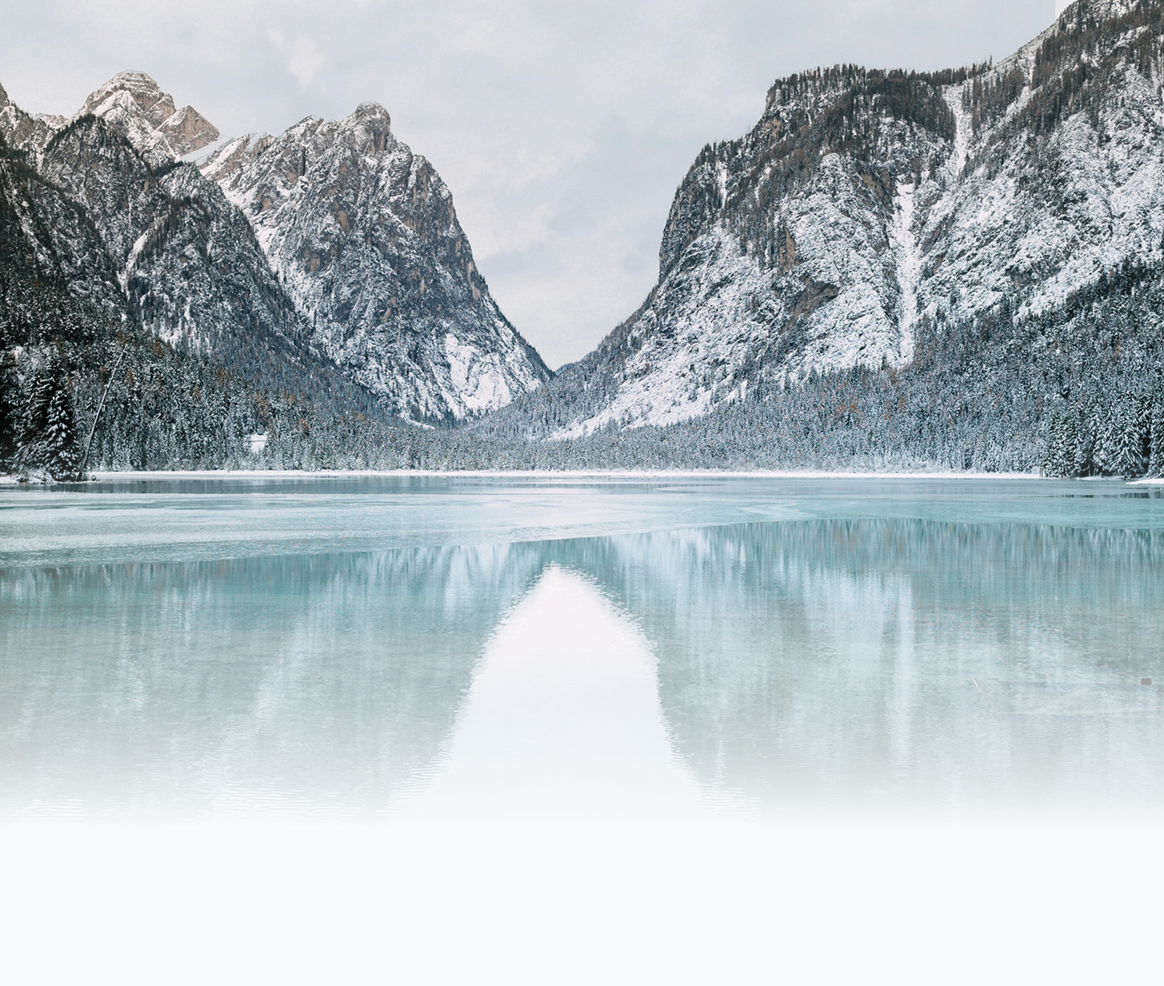 Snow-covered mountains and trees reflected in a partially frozen lake.