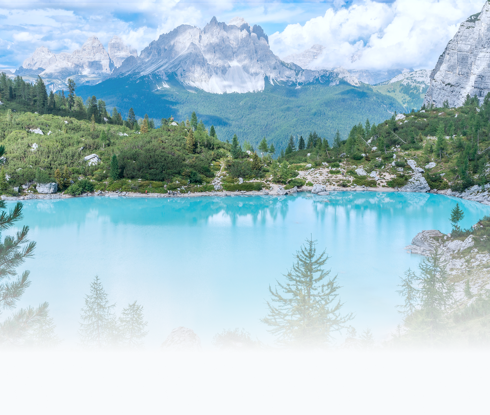 A mountain landscape featuring rugged peaks, green forests, and a bright turquoise lake under a partly cloudy sky.