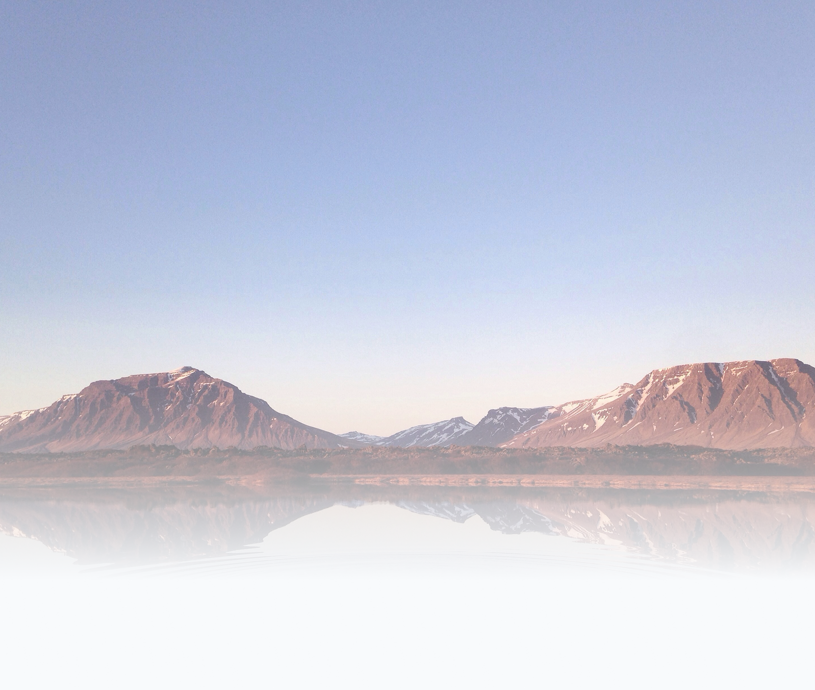Mountains reflecting on a calm lake with clear sky above.
