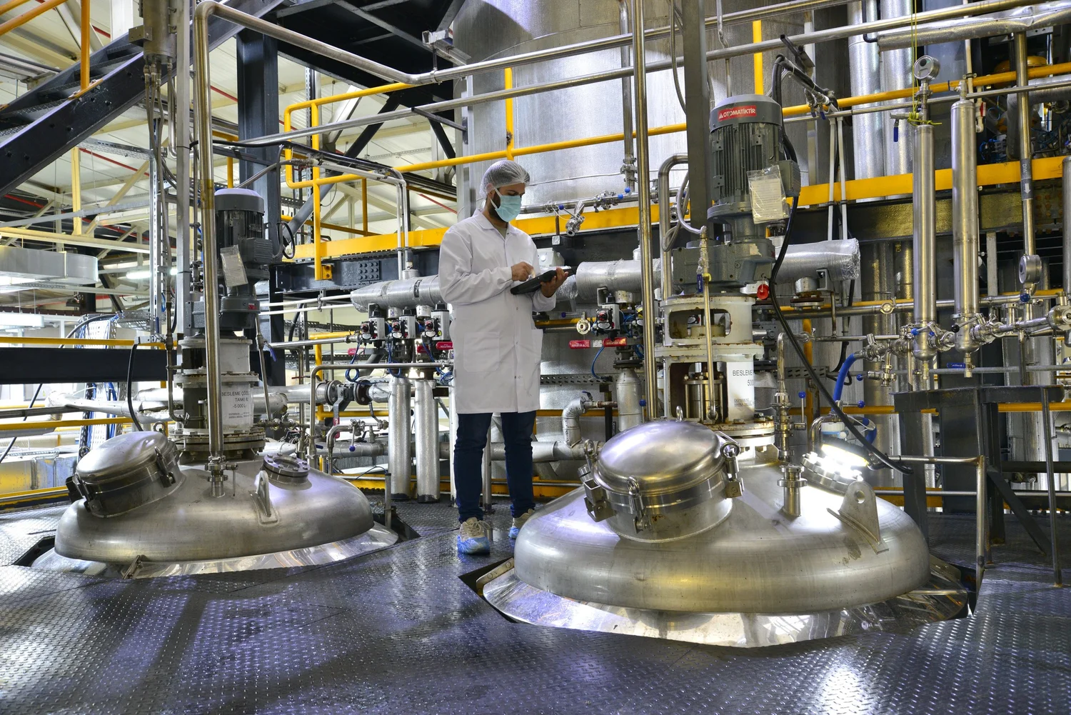 An operator in a lab coat and hairnet standing among the production fermenters in Livzym's fermentation hall