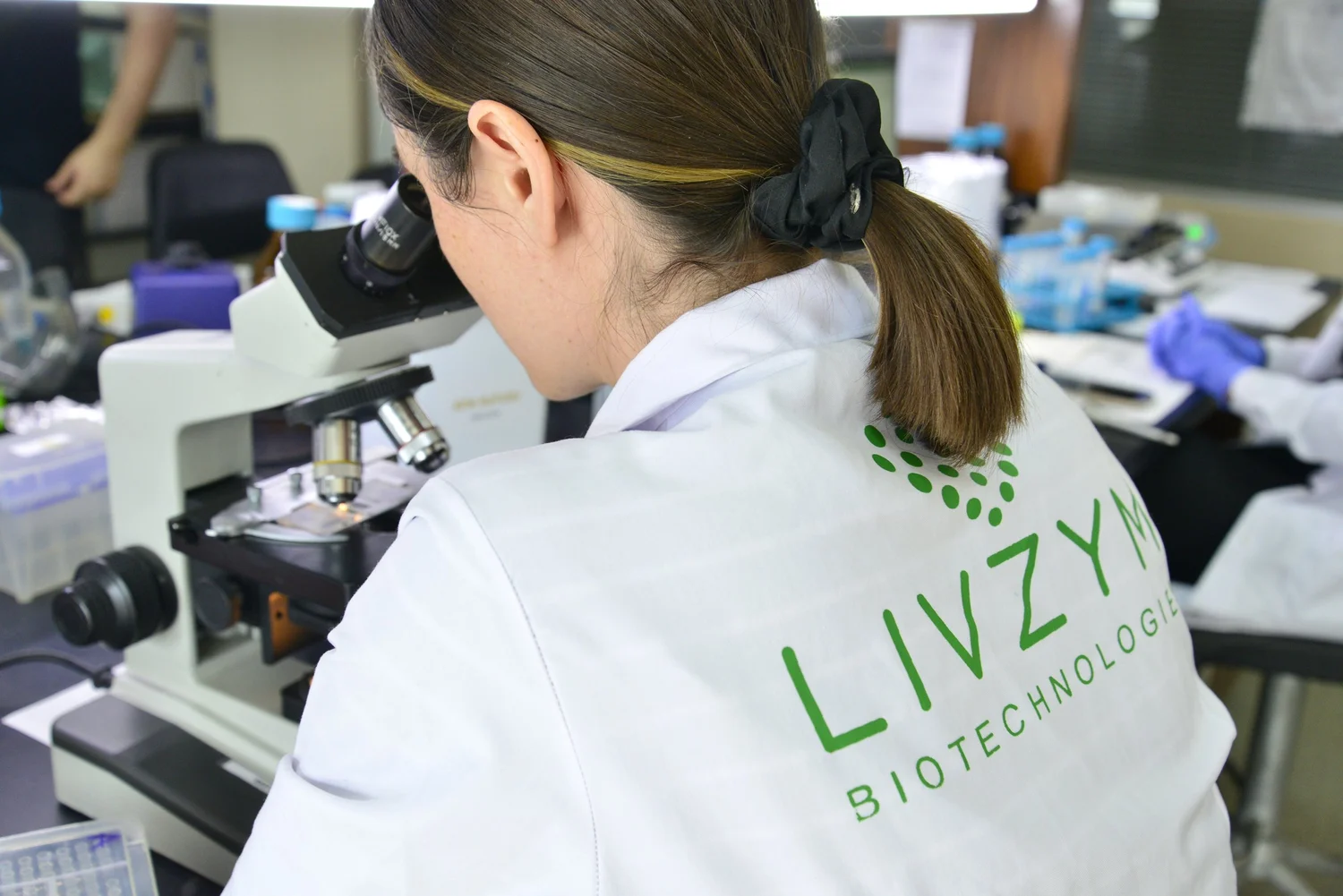 A Livzym scientist in a lab coat examining a sample under a microscope in the molecular biology laboratory