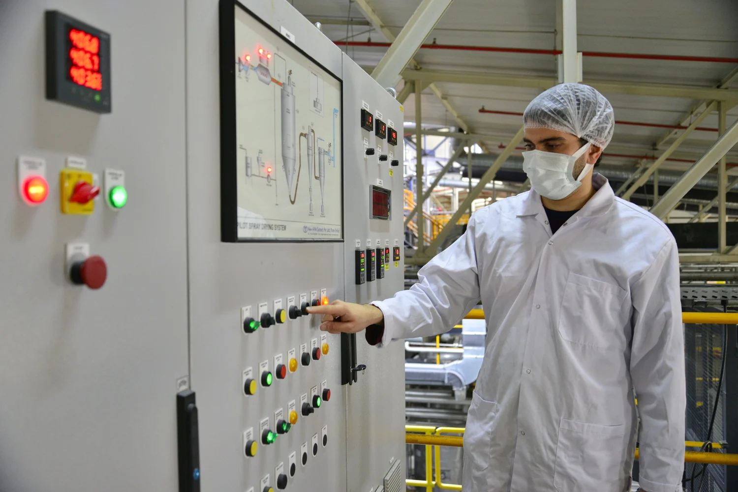 A Livzym operator in a lab coat and hairnet at a process control panel in the production plant