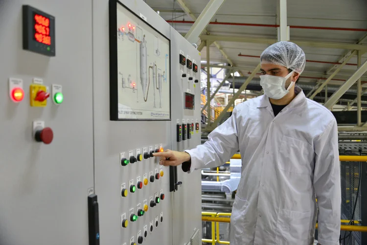 An operator in a lab coat and hairnet at a process control panel
