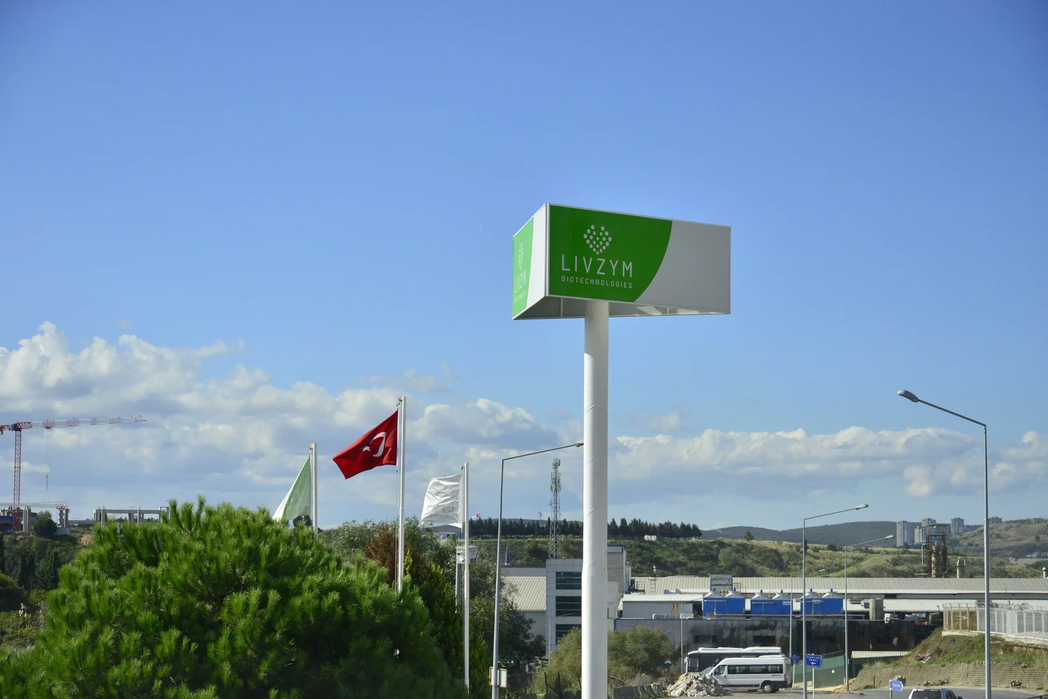 The Livzym sign on a tall post at the entrance of the facility, with the Turkish flag and the plant behind