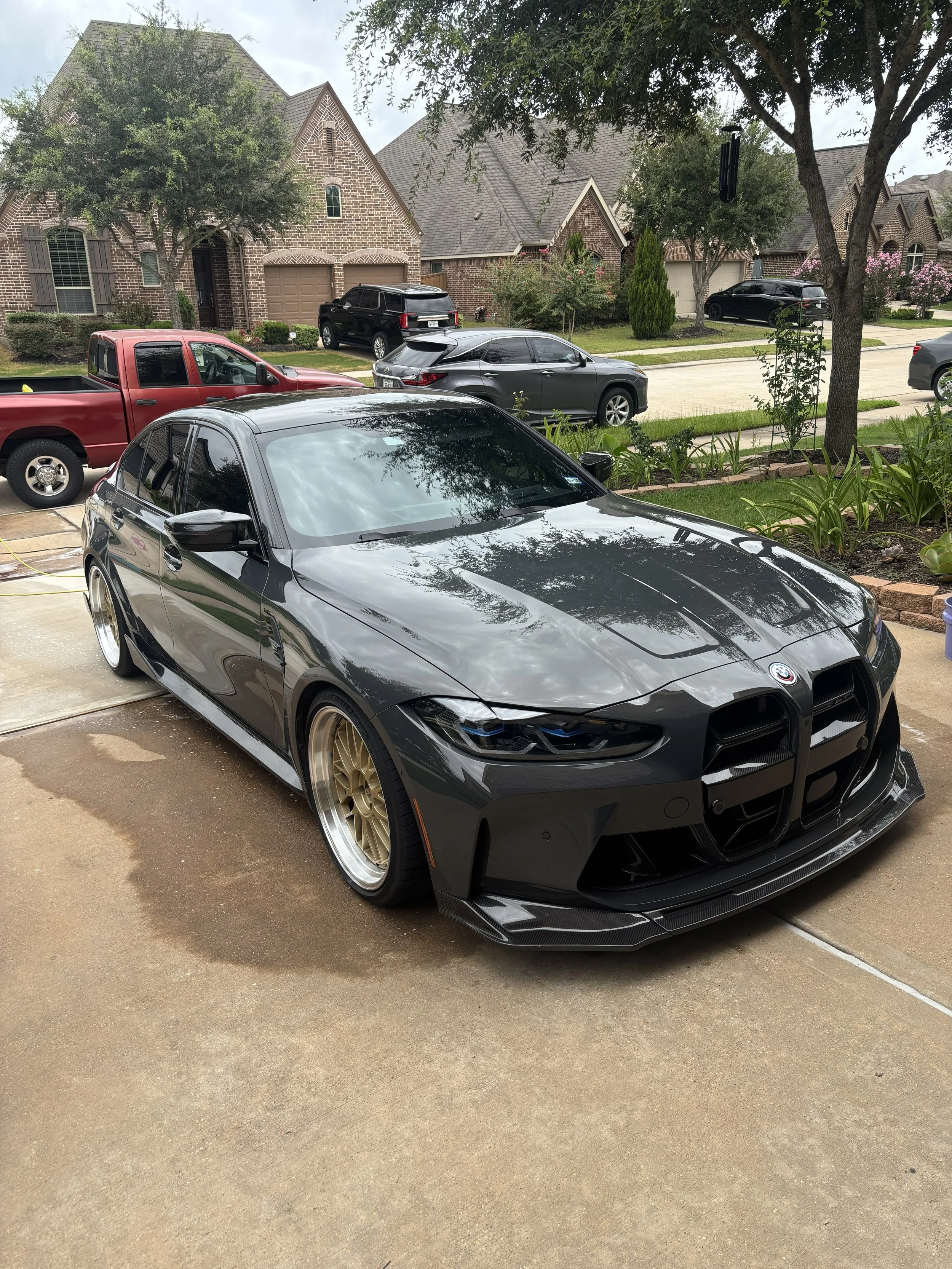 A black sports car with gold rims parked in a residential driveway.
