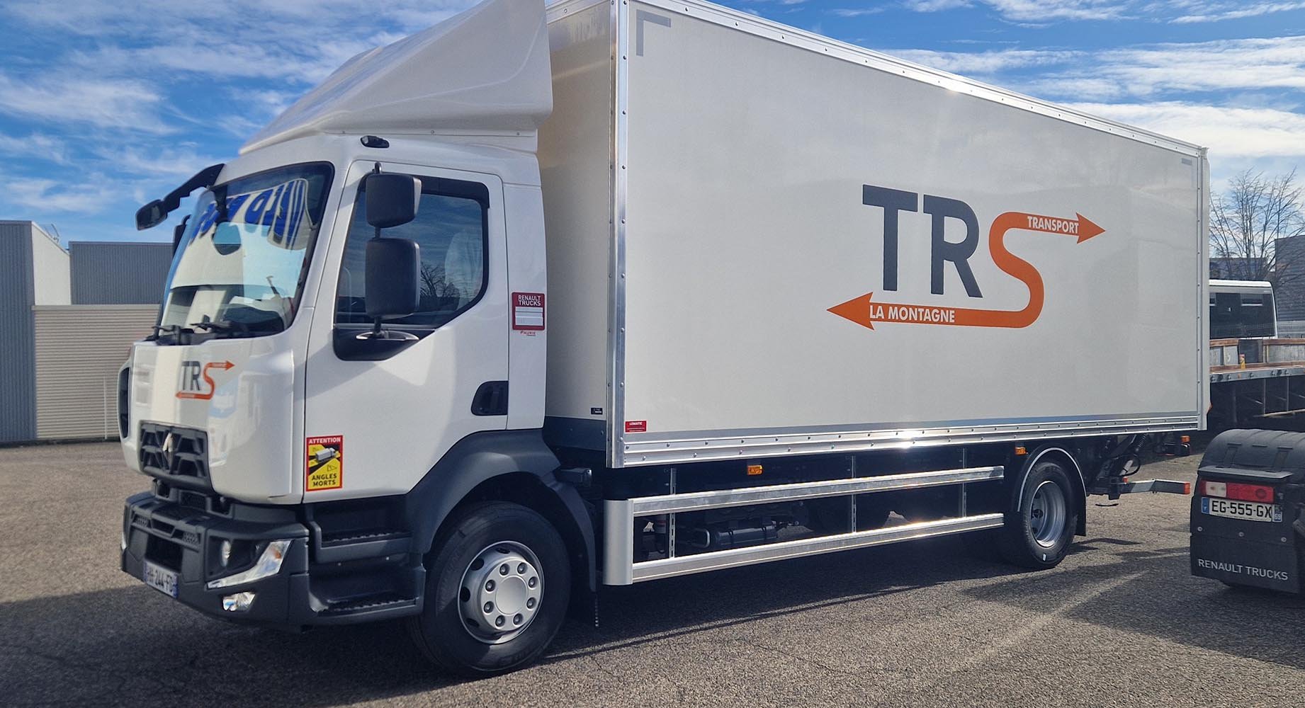 Camion de livraison blanc avec logo 'TRS Transport' et flèches oranges indiquant 'La Montagne' et 'Transport'.