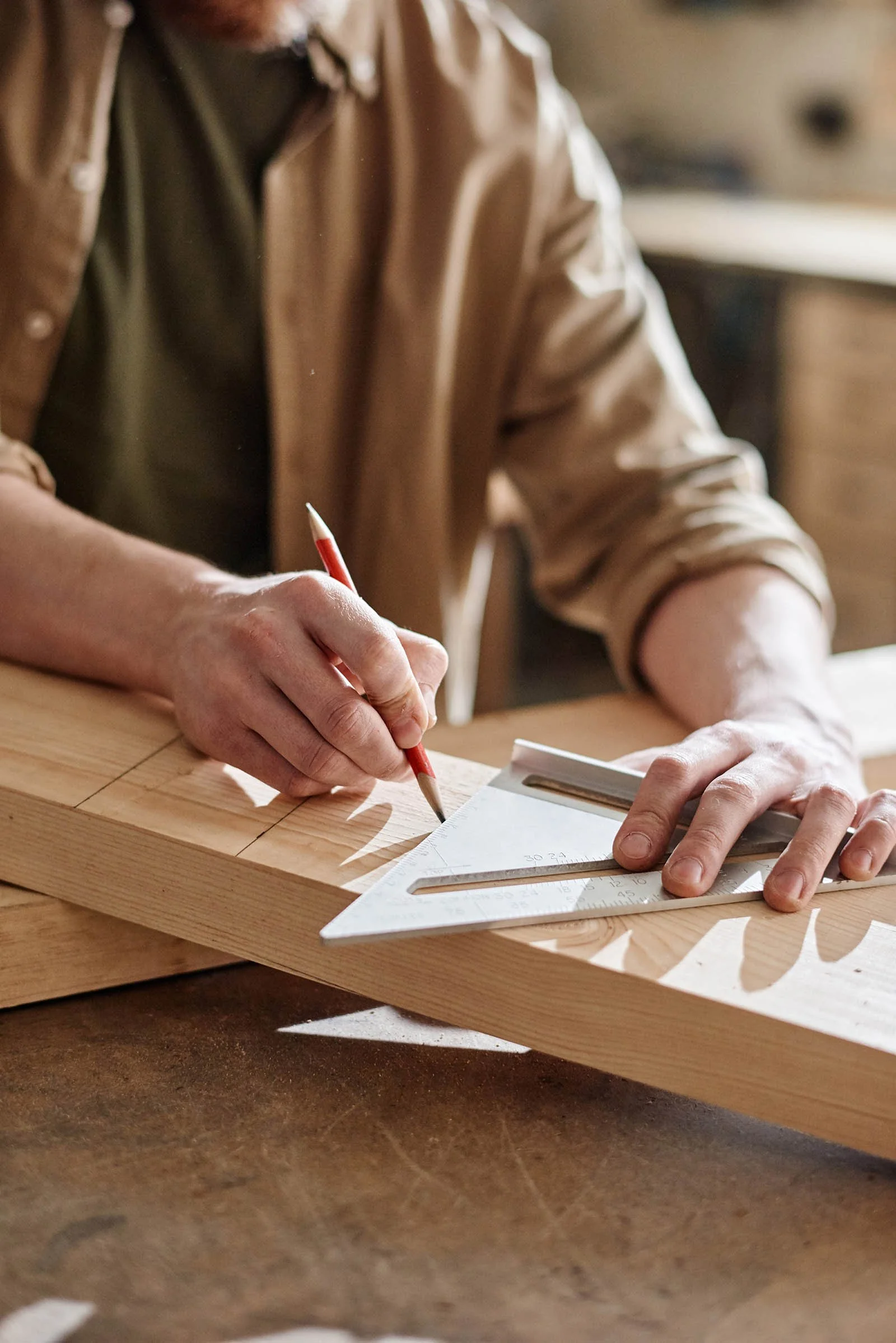 Une personne fait des dessins techniques sur une planche en bois à l'aide d'une équerre et d'un crayon.