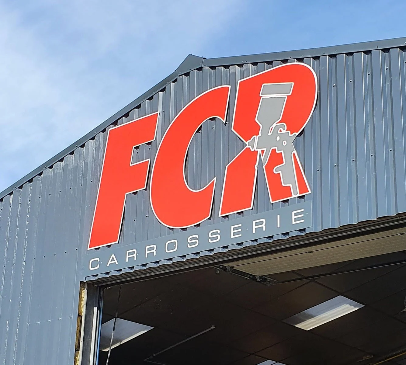 Panneau de signalisation d'une carrosserie automobile avec le texte 'F.C.I. Carrosserie' écrit en grandes lettres rouges sur fond gris métallisé.