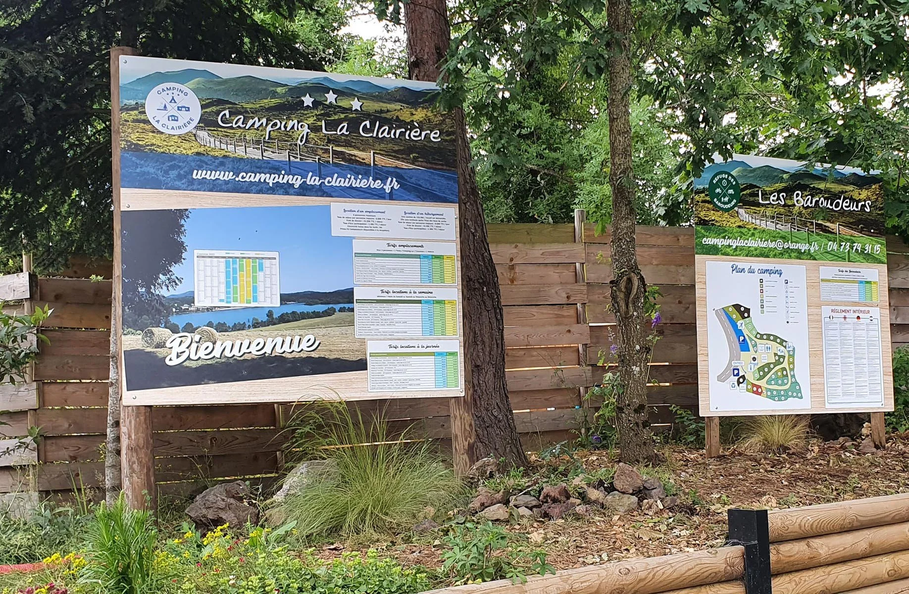 Tableau d'informations sur le camping La Clairière avec un plan du camping, une carte des emplacements, et des règles intérieures, installé dans un environnement arboré.