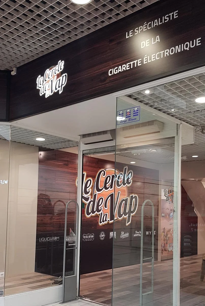 Façade d'une boutique de cigarettes électroniques appelée 'Le Cercle de la Vape' avec une enseigne lumineuse et un logo décoratif, située dans un centre commercial.