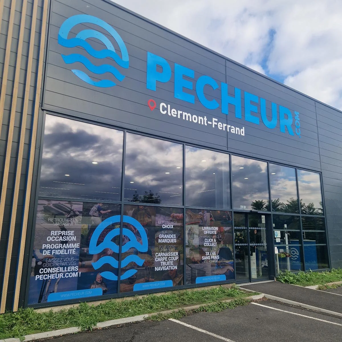 Façade d'une boutique de pêche appelée pecheur.com à Clermont-Ferrand, avec de grandes fenêtres et un panneau avec le logo et des informations.