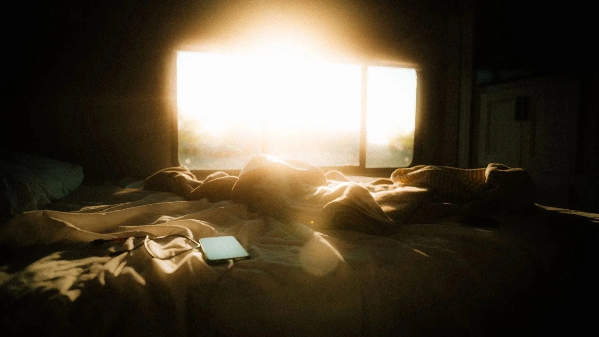 a phone charging in bed with a bright sunlight coming from the window
