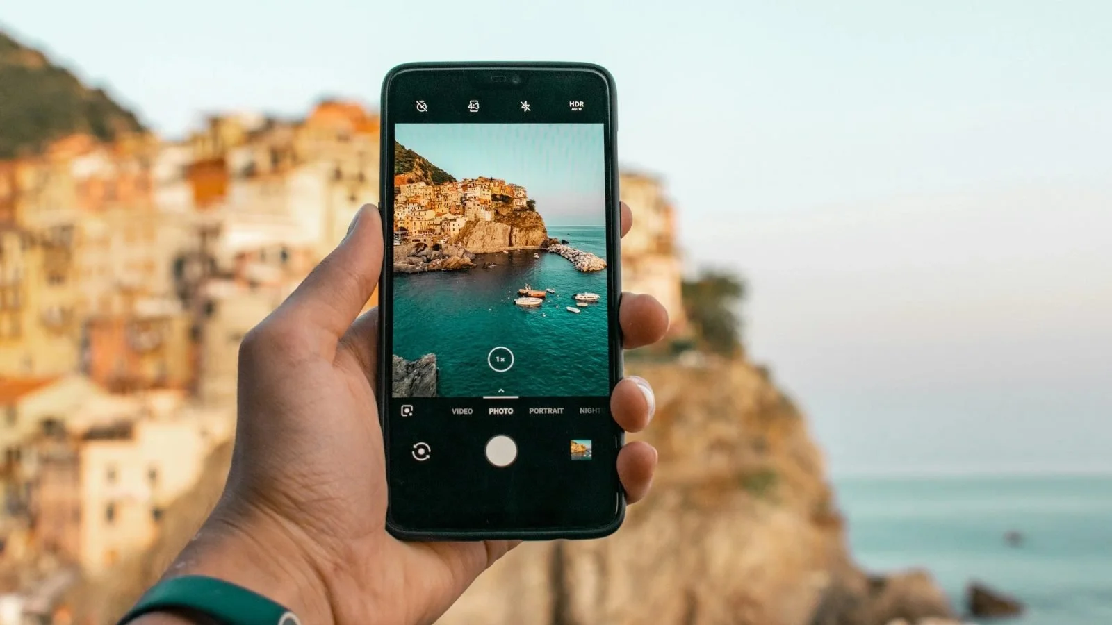 Hand holding a smartphone while taking a photo of a seaside town