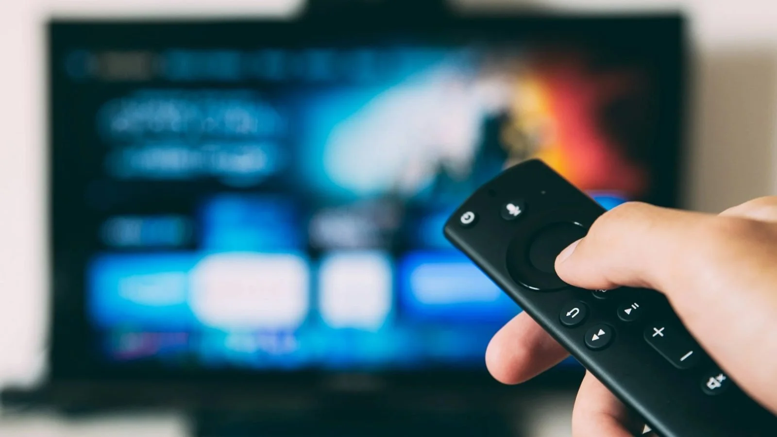 Hand holding a TV remote in front of a smart TV home screen with streaming recommendations