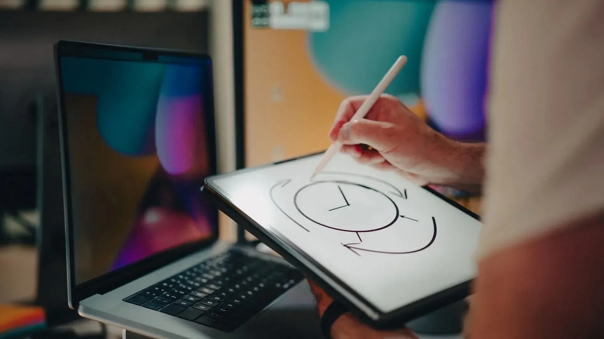 Graphic designer drawing on a tablet with a stylus next to an open laptop