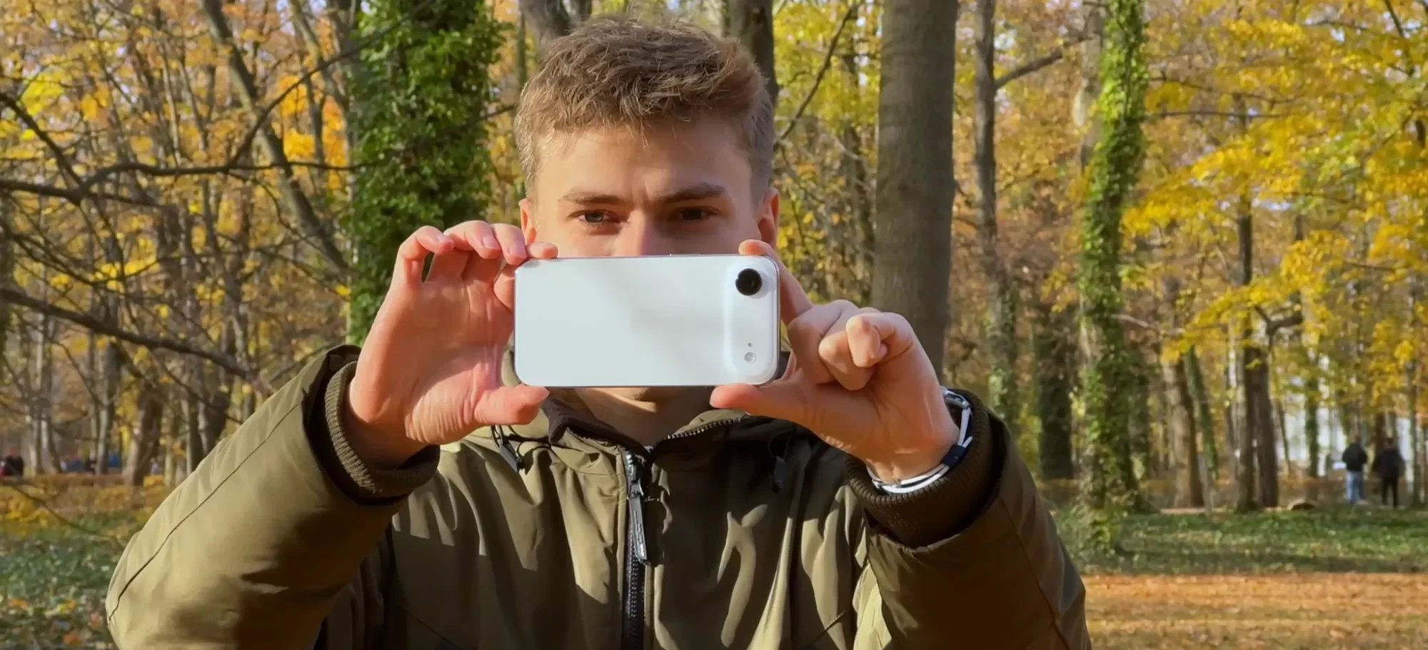 Man holding up an iPhone Air to take a photo in an autumn park