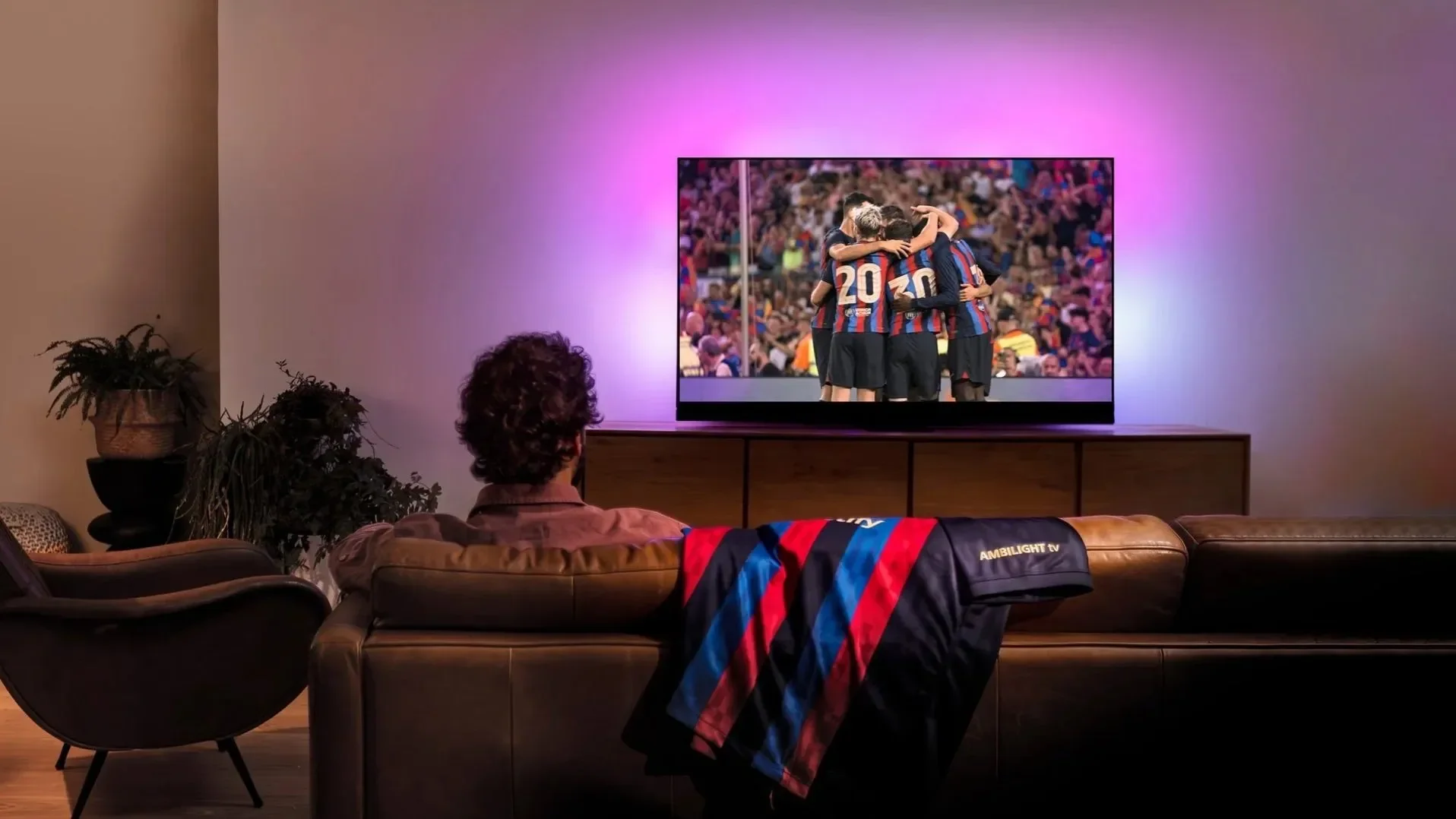 People watching football on a TV with a purple Ambilight glow in a dark living room